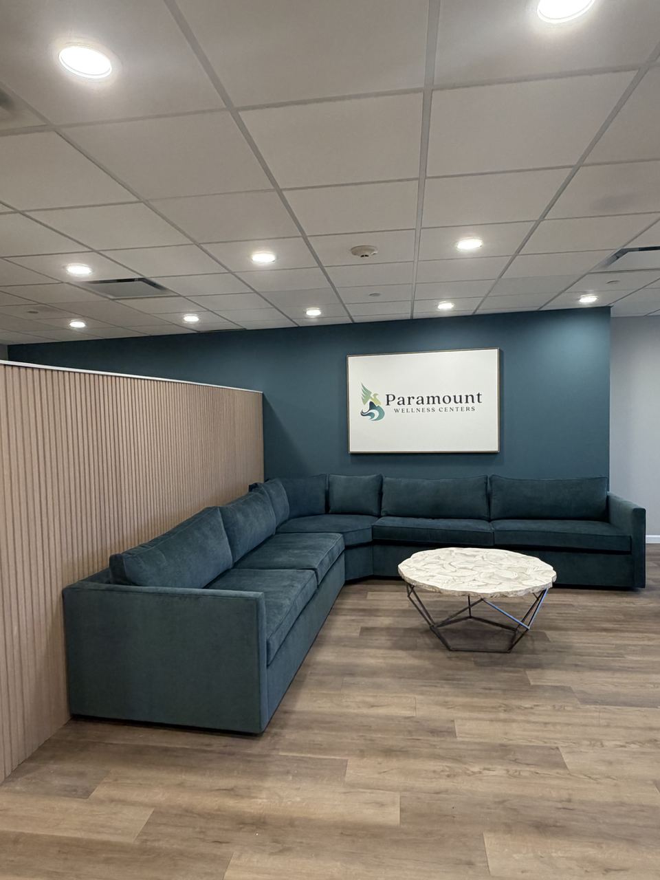 Waiting lounge with sectional sofa and Paramount Wellness Centers sign at the Stamford office