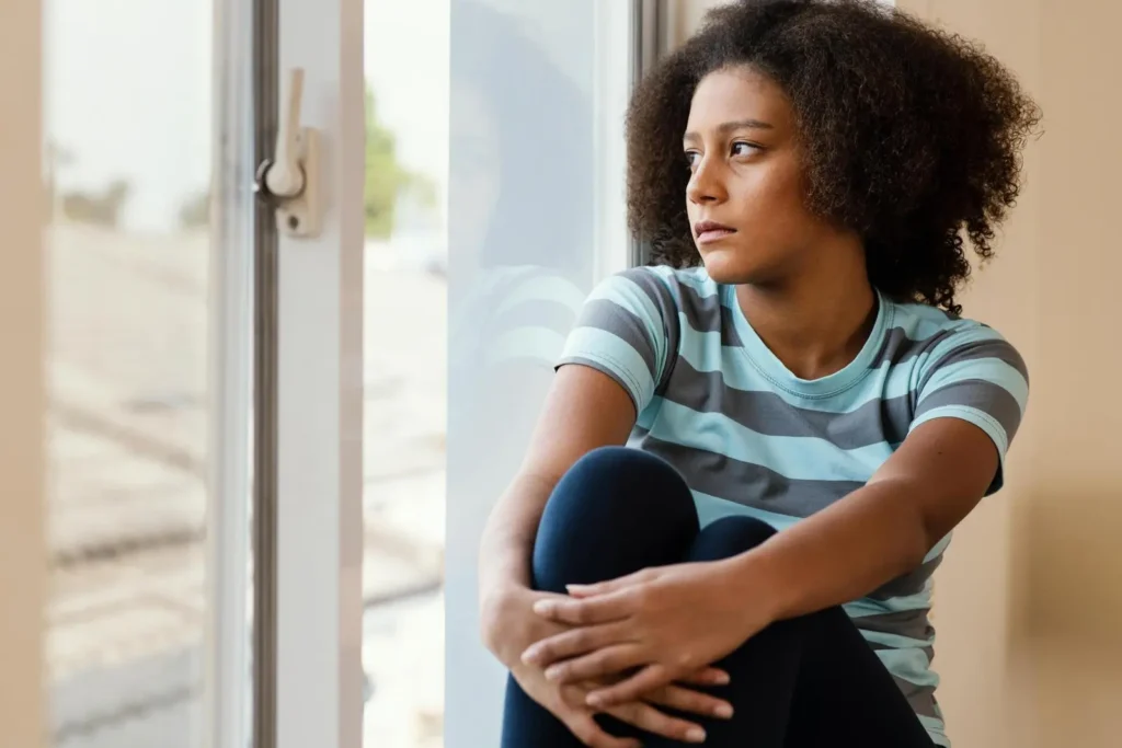 BIPOC Therapist Benefits - A women with her knees pulled up while looking out a window.