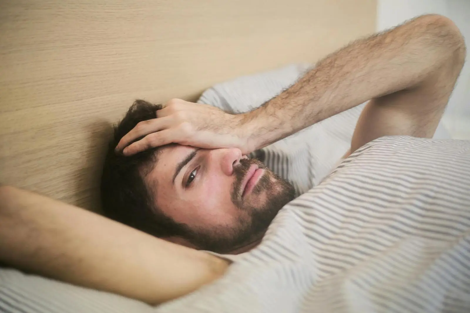 Does NyQuil Make You Sleepy? A man laying in bed with his hand covering half of his face.